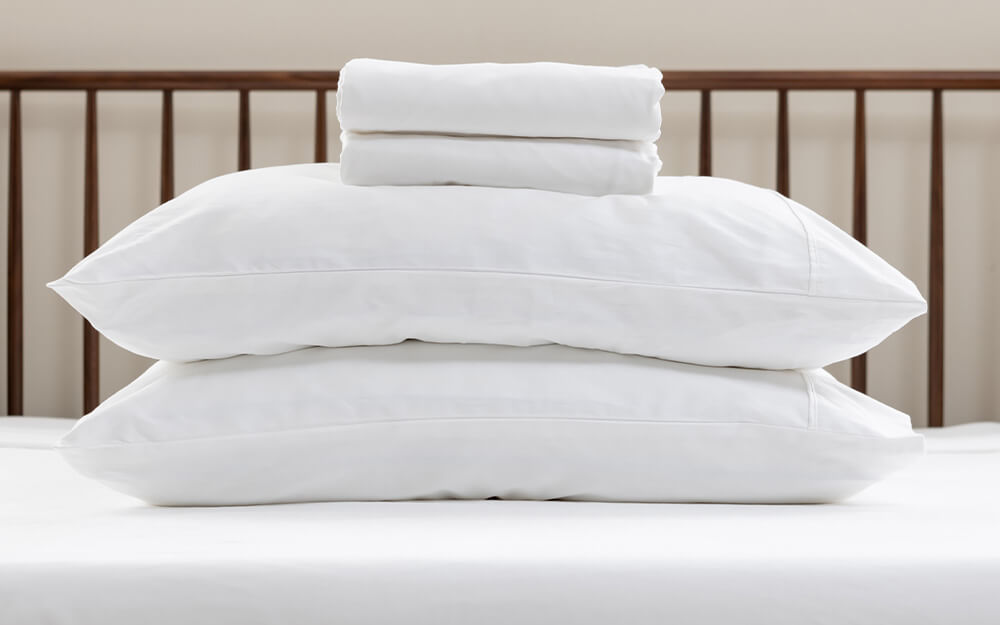 Draps en satin de coton sur deux oreillers, empilés sur un lit