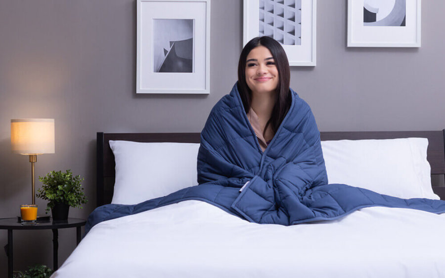 Woman seated in bed with Classic Weighted Blanket hugged around her shoulders