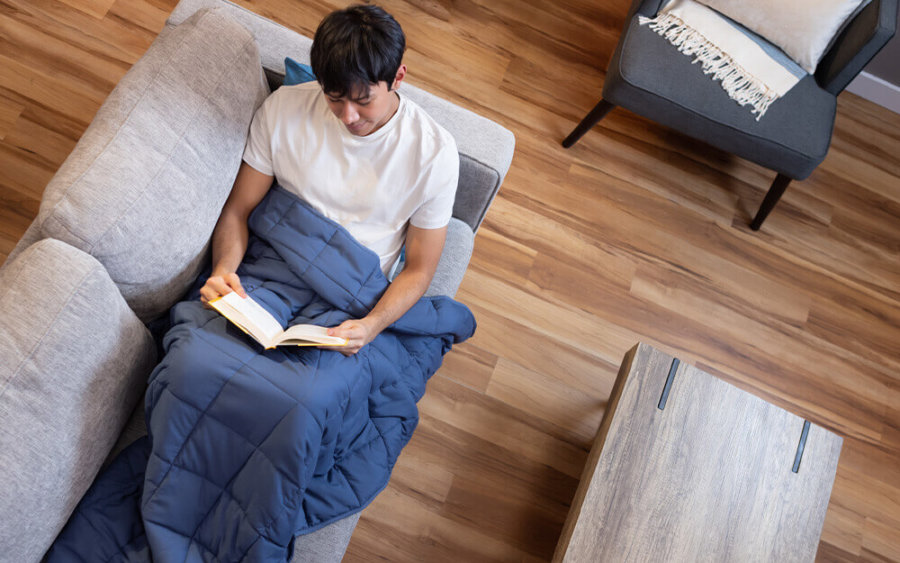 Man reading a book on the couch, with Classic Weighted Blanket draped over his lower body