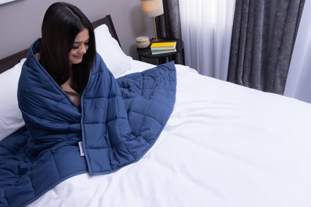 Woman smiling serenely as she hugs herself with Classic Weighted Blanket draped over her shoulders