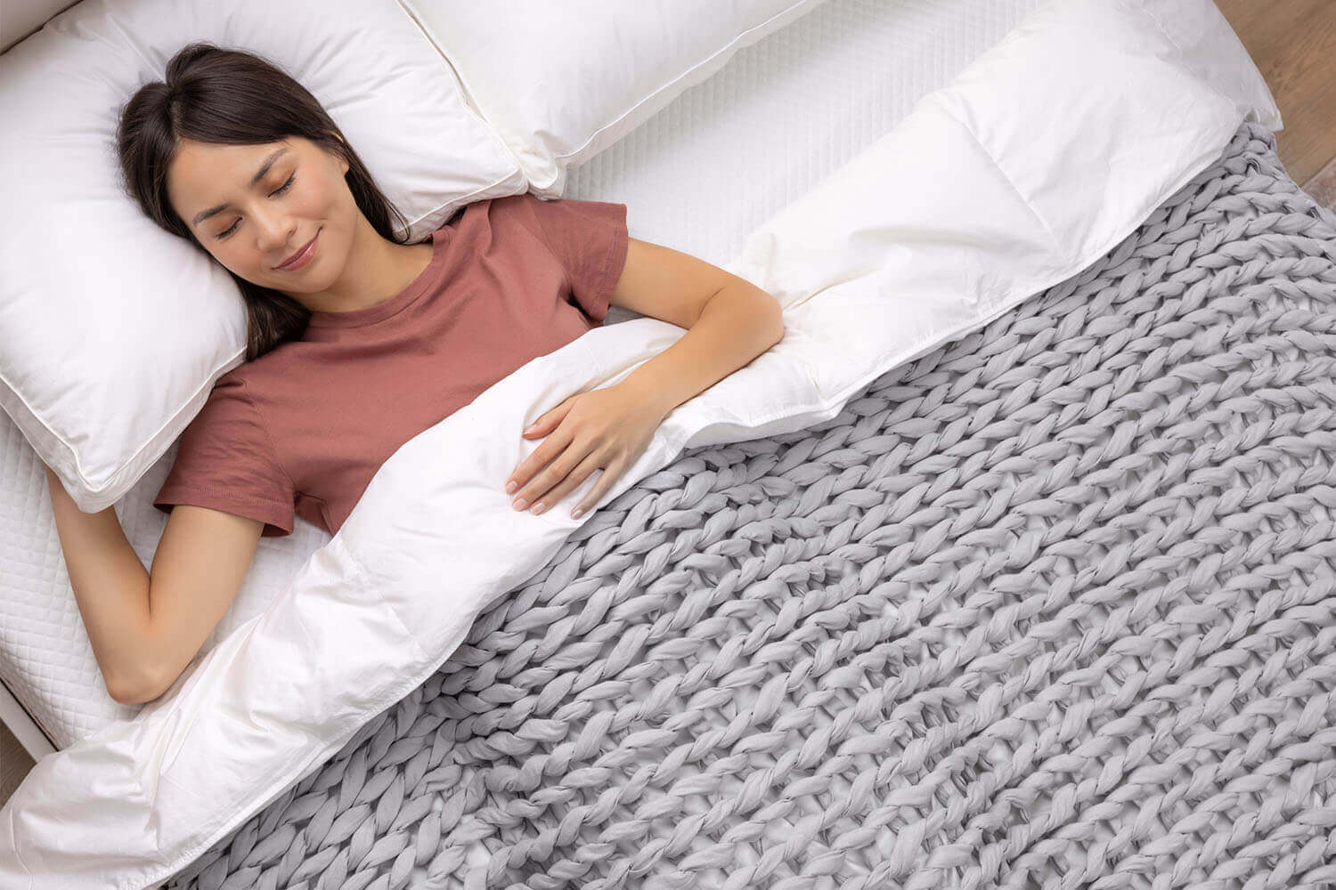 Woman lying on her back in bed, with the Douglas Hand Knit Weighted Blanket hugging her body